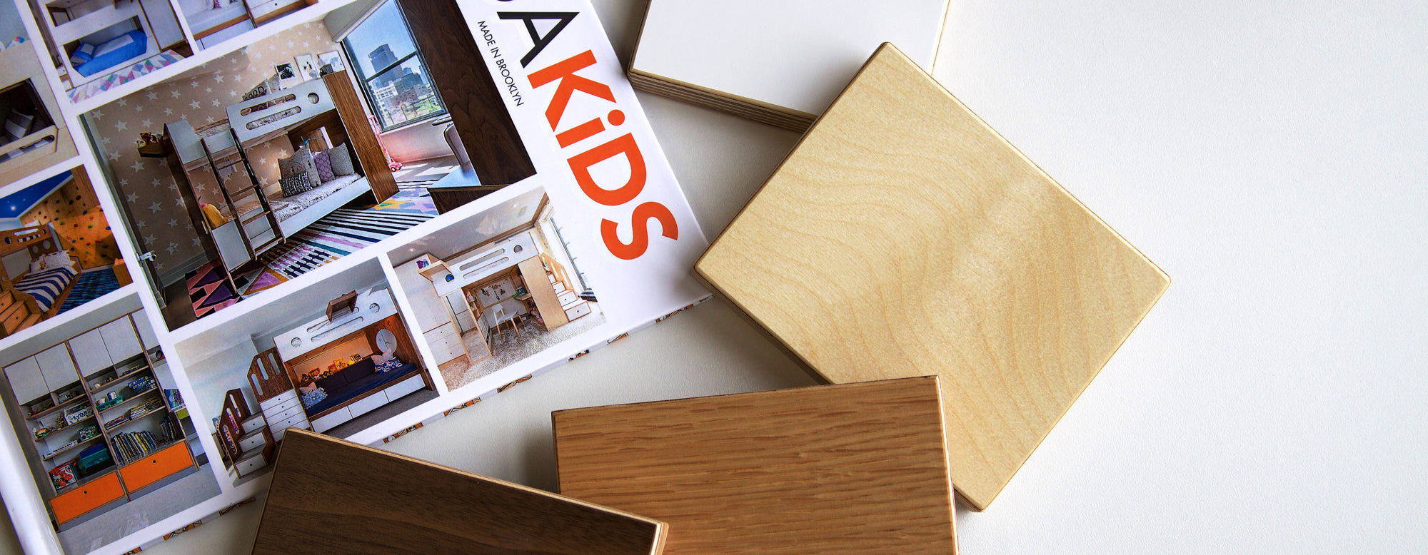 Open magazine featuring interior designs next to wood samples on a white surface.