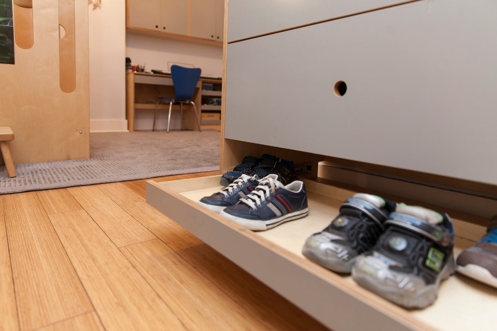 Low-angle view of shoes on a shelf under furniture in an indoor setting.