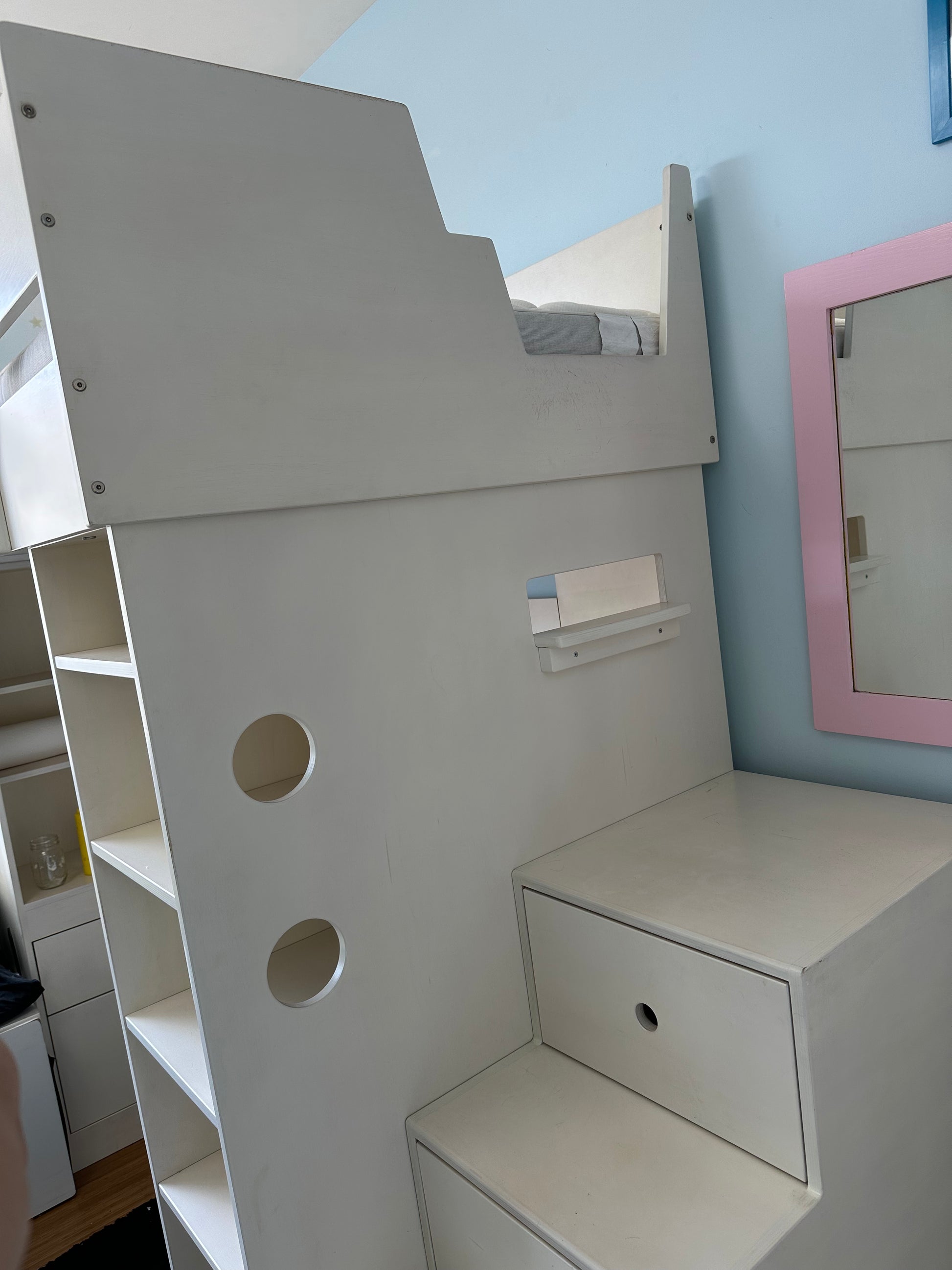 White children's playhouse with shelves and a small desk against a light blue wall.