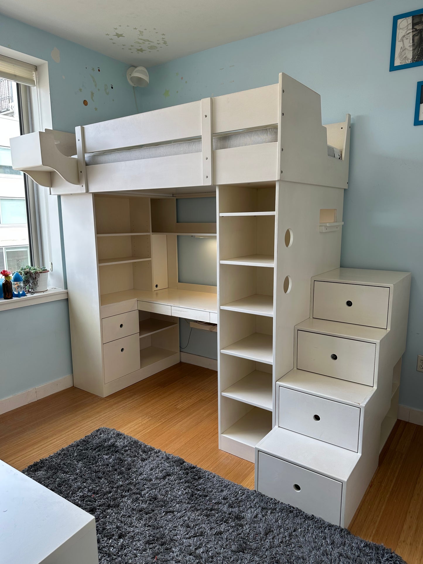 White loft bed with desk and shelves in a room with blue walls and a window.