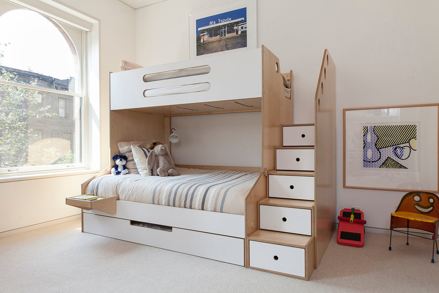 A wooden bunk bed with stairs, storage drawers, and toys, in a bright room with a large arched window and artwork on the walls.