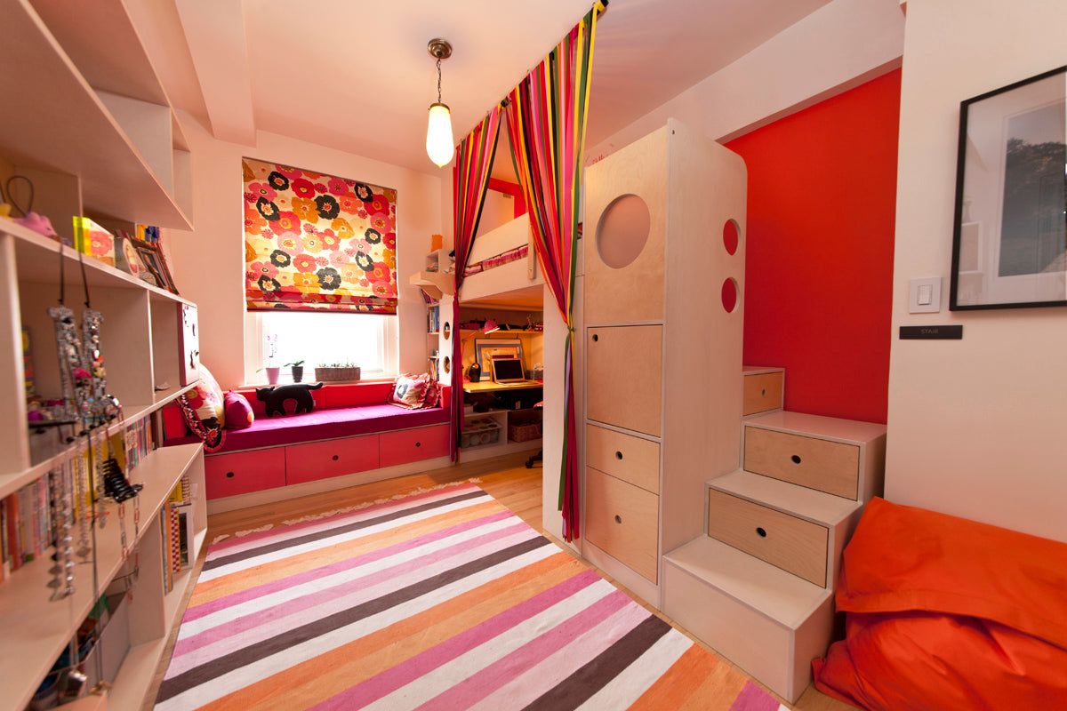 A colorful kids' room with a wooden bunk bed, steps, a vibrant striped curtain, a window seat, and a striped rug.
