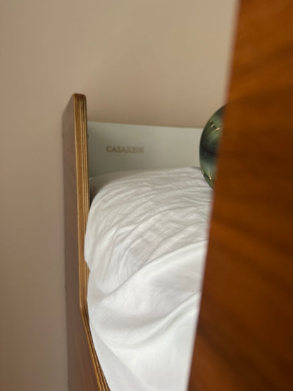 A close-up view of a bunk bed with a wooden frame and casa kids logo engraved near the top, photographed indoors against a beige wall.