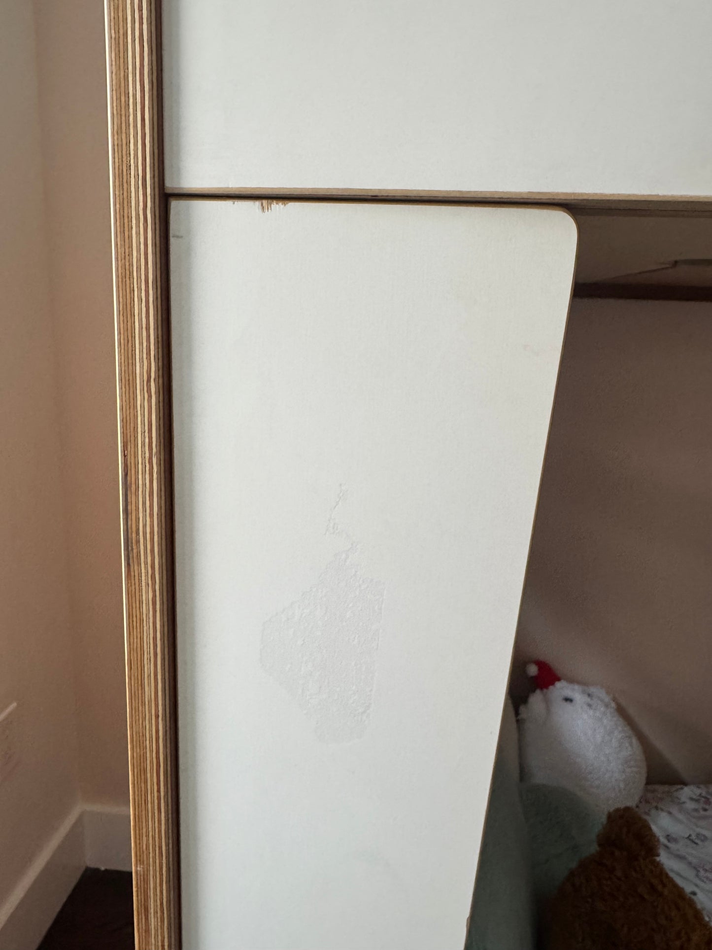 A close-up of a white wooden furniture piece, showing a panel with faint scuffs and scratches, alongside a light wood frame.