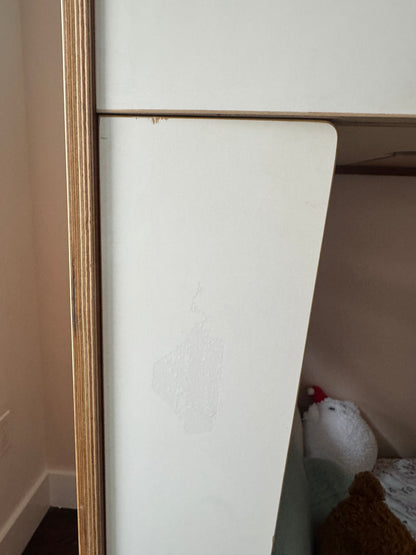 A close-up of a white wooden furniture piece, showing a panel with faint scuffs and scratches, alongside a light wood frame.