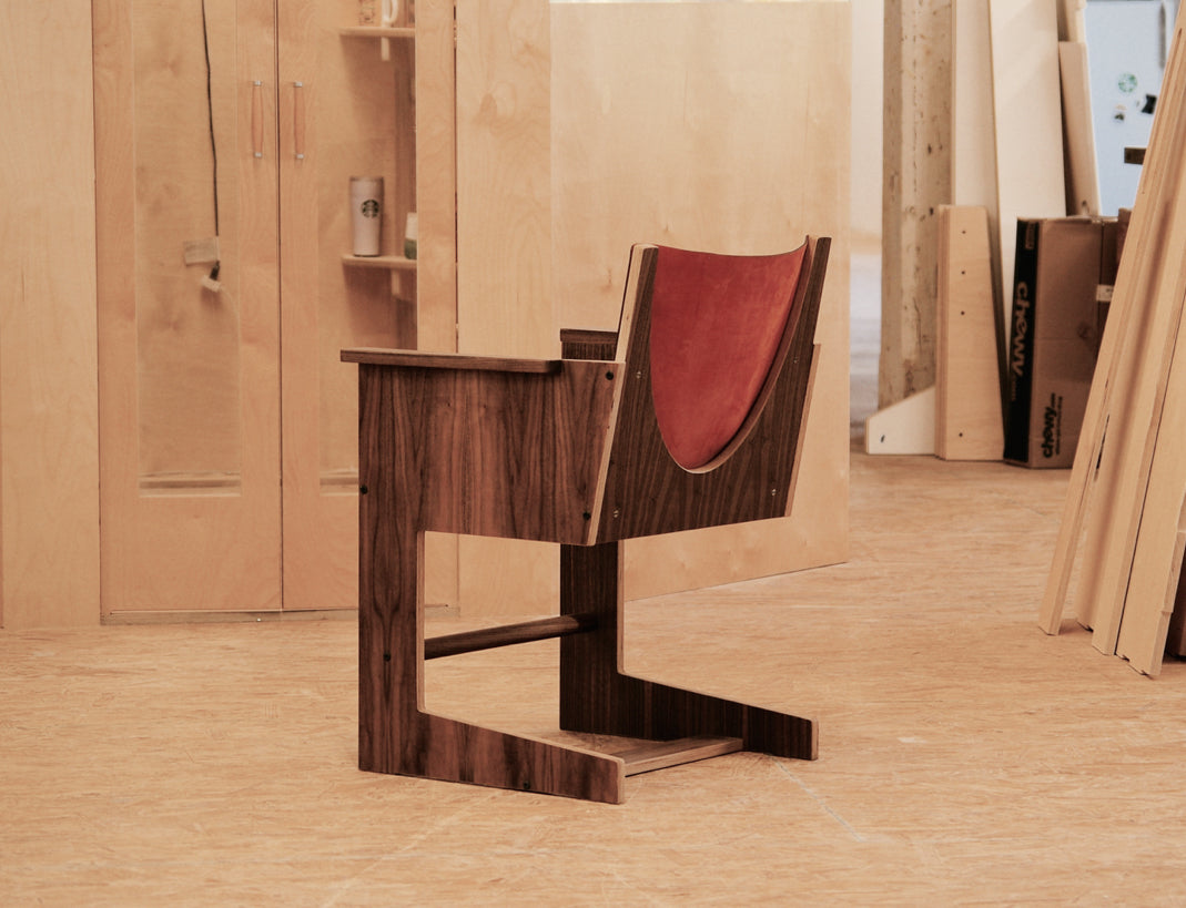 Stylish dark wooden chair with a red leather backrest set in a plywood workshop environment.