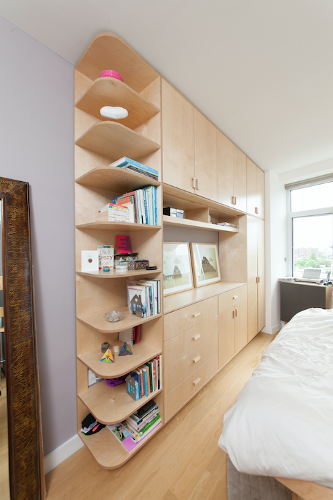 Sleek bedroom with a unique curvy wooden bookshelf integrated with cabinets, near a large window.