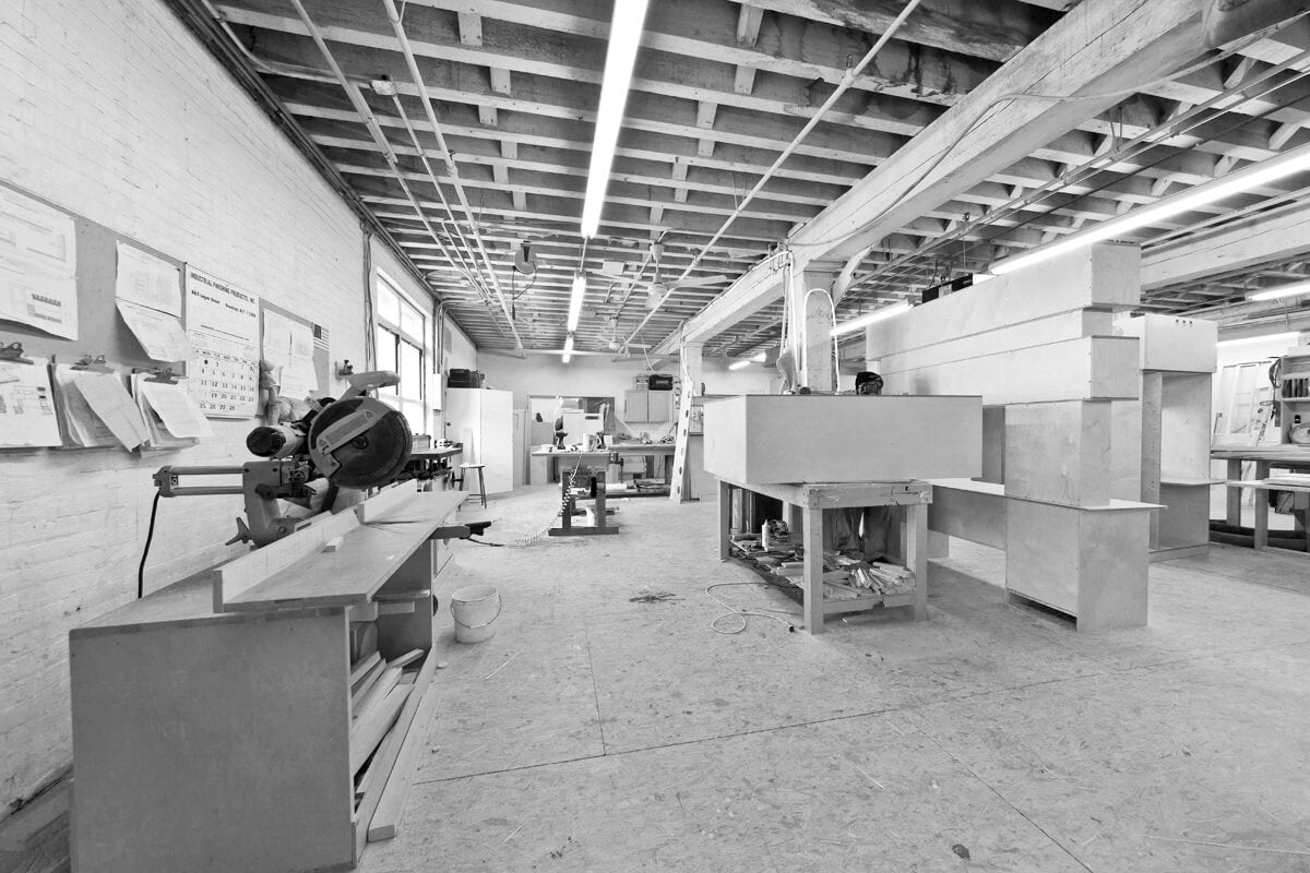 Black and white image of a busy workshop with people working and various machinery.