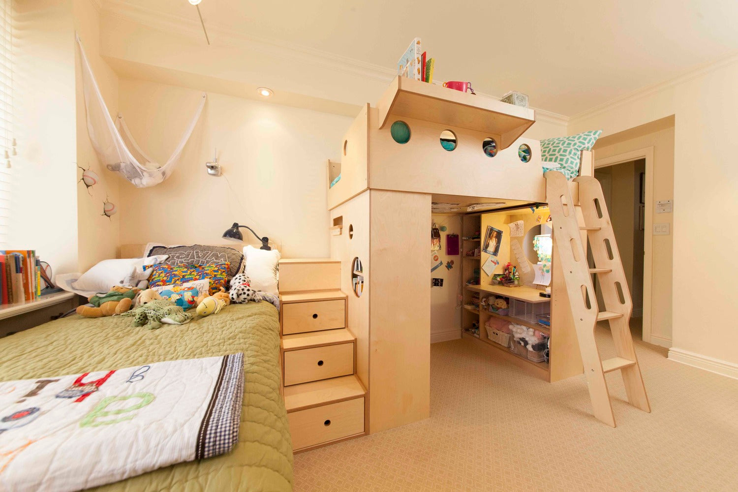 Children's room with a wooden loft bed, slide, and stairs, a lower play area with a desk, shelves, and toys, and a cozy bed.