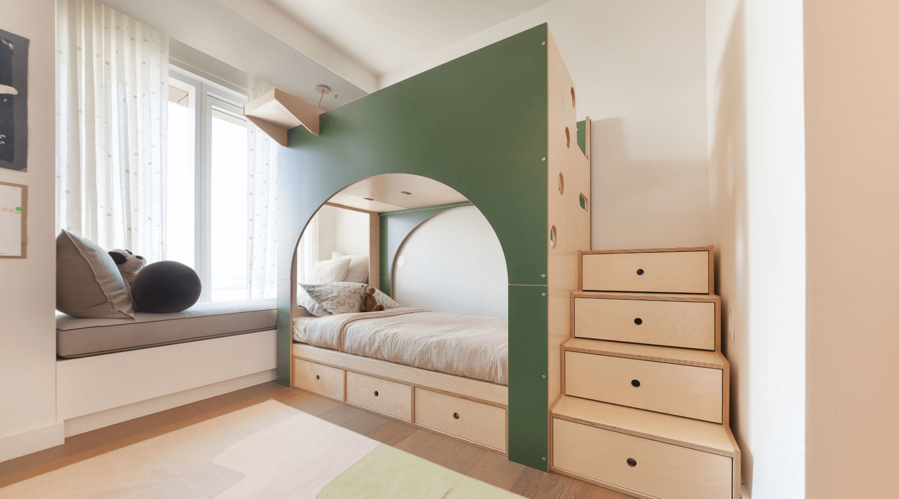 Modern childrens bedroom with a green arched bed nook built-in drawers and a window seat