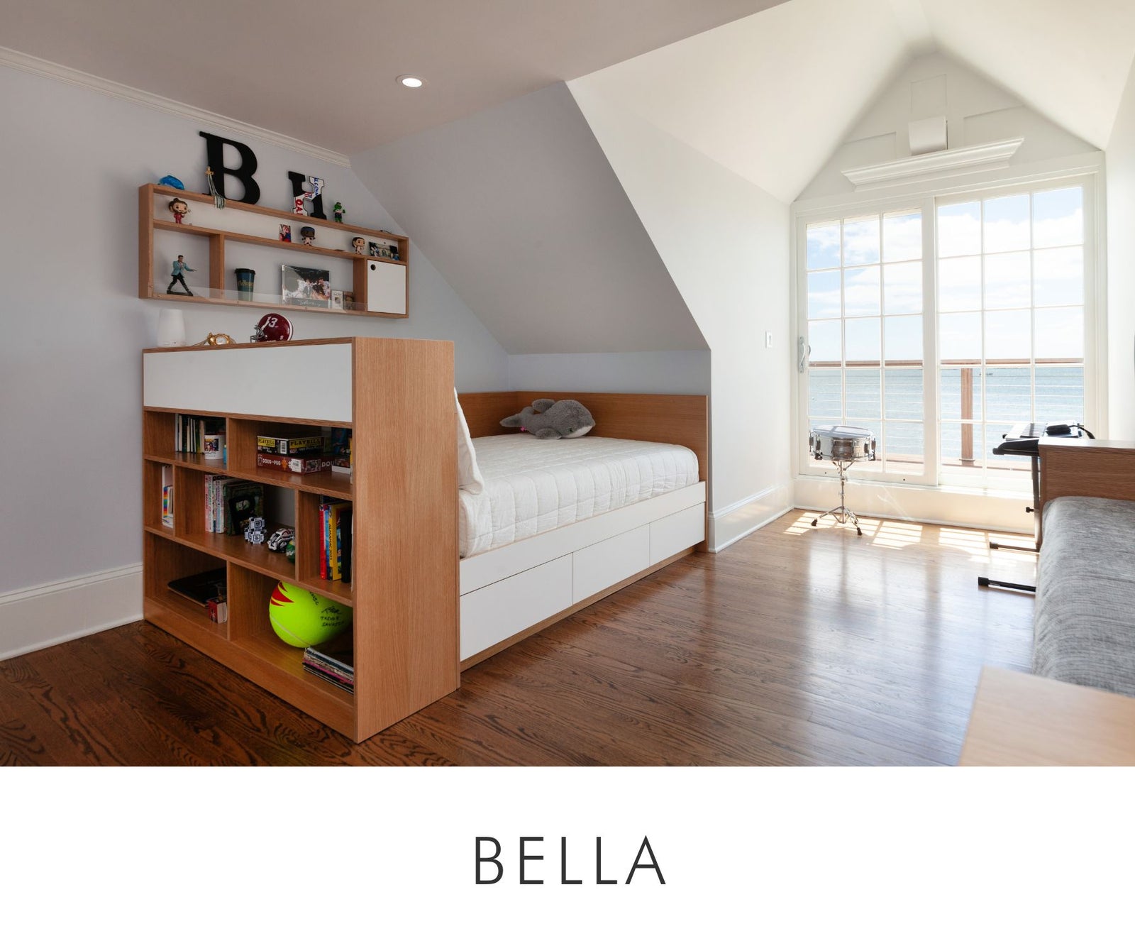 Custom full-size bed in white oak with white drawer storage, paired with an open cubby bookshelf and wall-mounted display shelf — designed for bright, organized kids’ rooms with a view.
