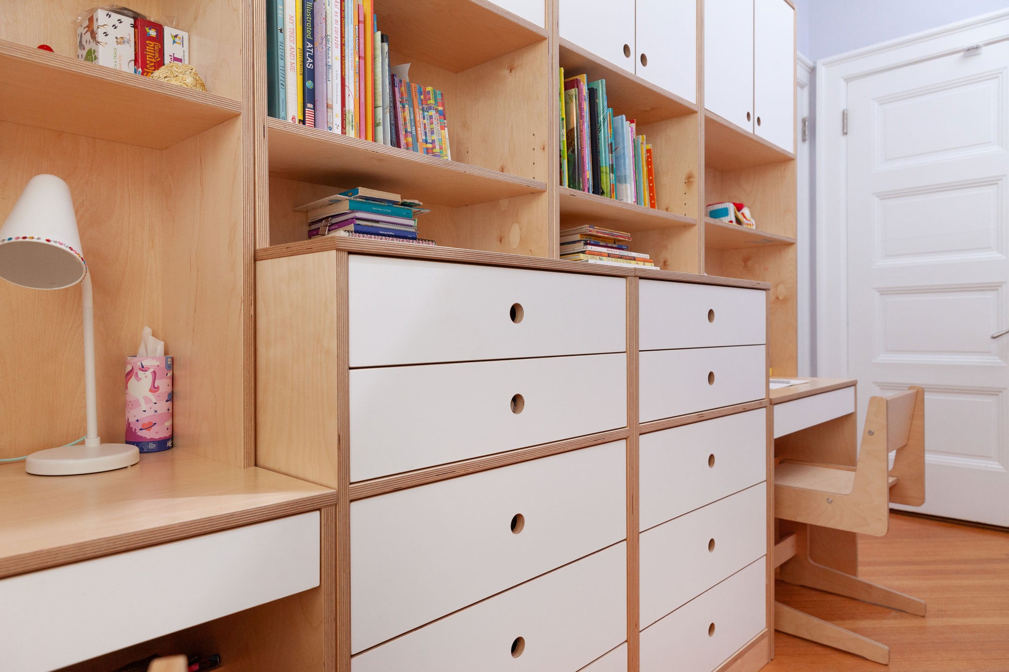 Birch shelving unit with white drawers and a desk, featuring books and toys in a child's bedroom.

