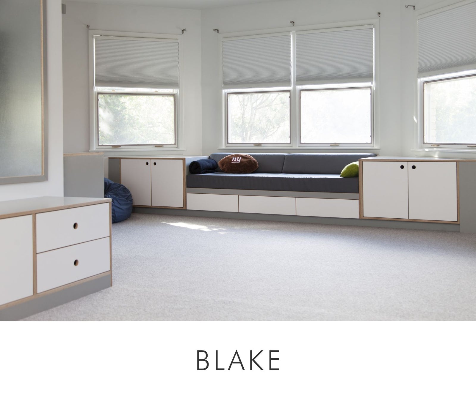 Contemporary kids' room bench with custom white and gray cabinetry, under-bench drawers, and soft upholstered seating in front of bay windows.
