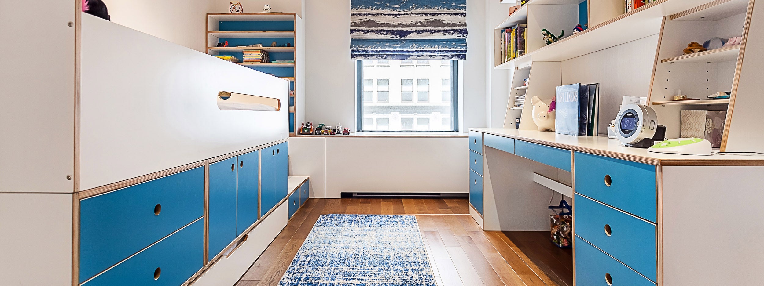 Modern child's room with a long white and blue storage unit and a study area facing a window.
