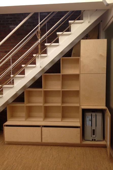 Cleverly designed under-stair storage with open shelves and drawers in a modern home with a metal railing.
