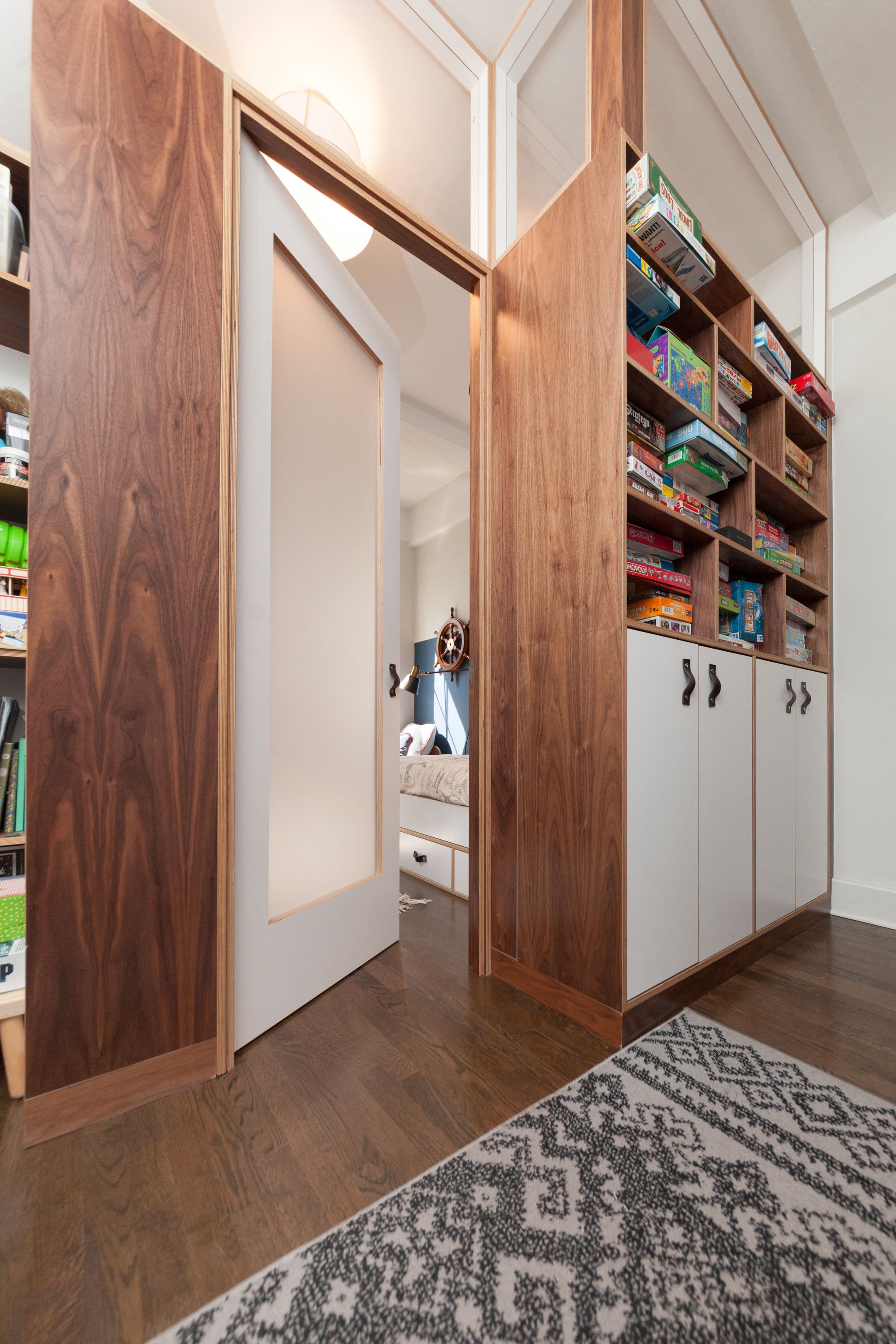 Custom walnut room partition with built-in shelving and storage, separating playroom and bedroom spaces.