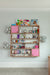 Custom wall-mounted shelving unit with white oak finish and pink painted accents, featuring headband storage, toys, and decorations in a bright children's room.

