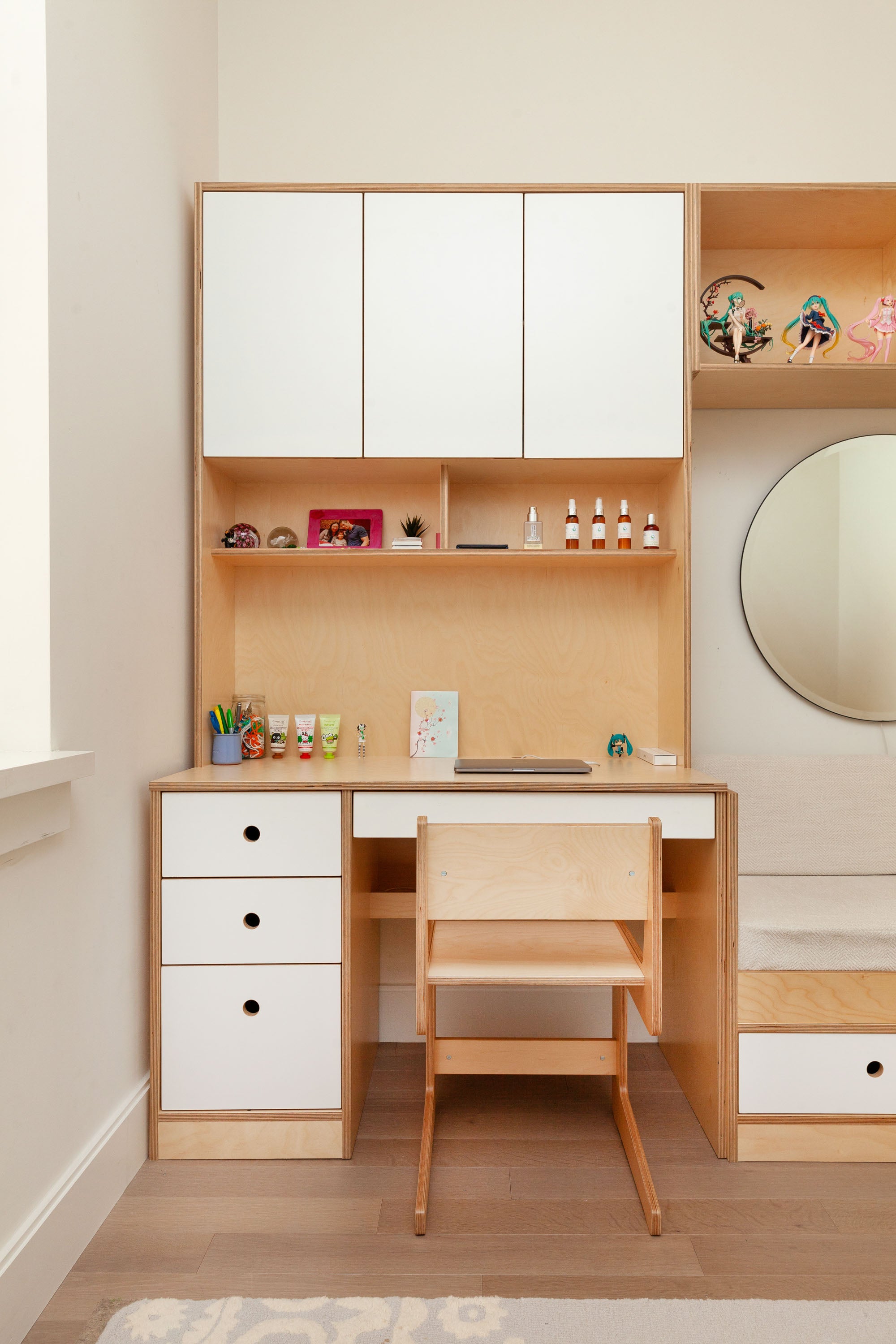 Compact desk unit with white oak finish and white painted accents, featuring a drawer set, upper cabinets, and open shelving for display. The desk includes a matching chair, creating a cohesive workspace.

