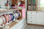 Headband display and shelving unit with pink accents, featuring a white oak finish with white painted cabinets in a children's room.

