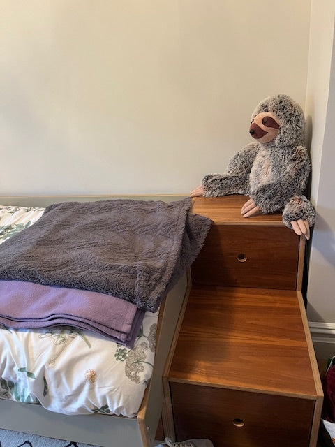 Dark wood nightstand or dresser with two drawers, next to a bed with a patterned duvet