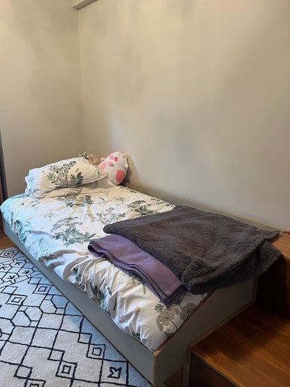 Single bed with raised storage base and wooden nightstand. Patterned blanket over a geometric rug