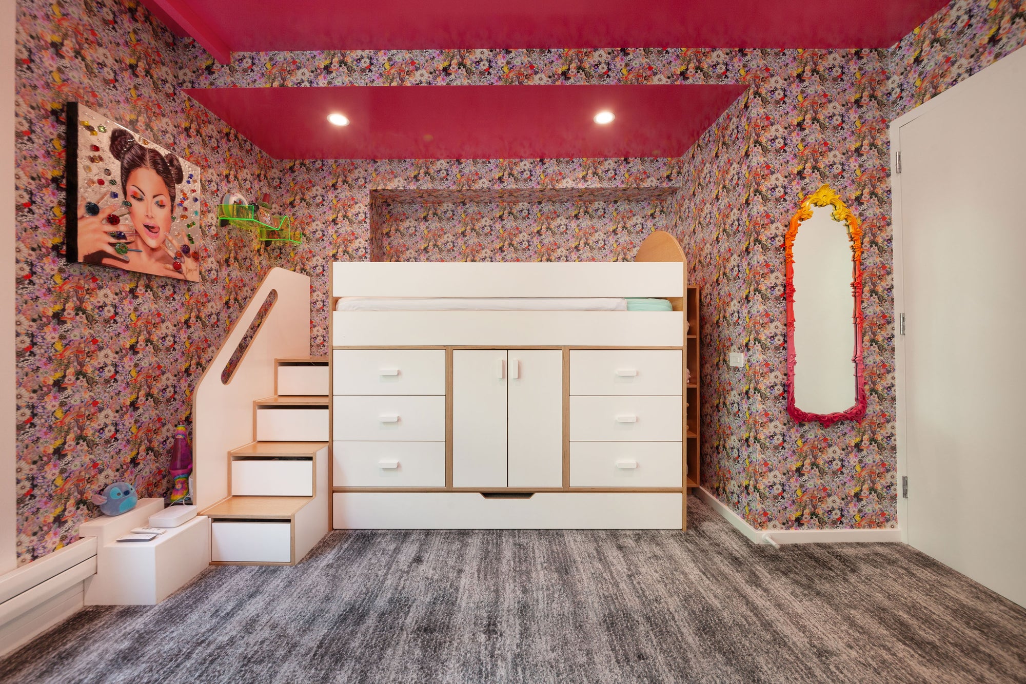 Vibrant children's bedroom featuring a loft bed with integrated storage drawers and cabinets in a white finish with birch accents. The room has a colorful floral wallpaper, a bold pink ceiling, and a staircase with additional storage steps, creating a lively and functional space for play and sleep.

