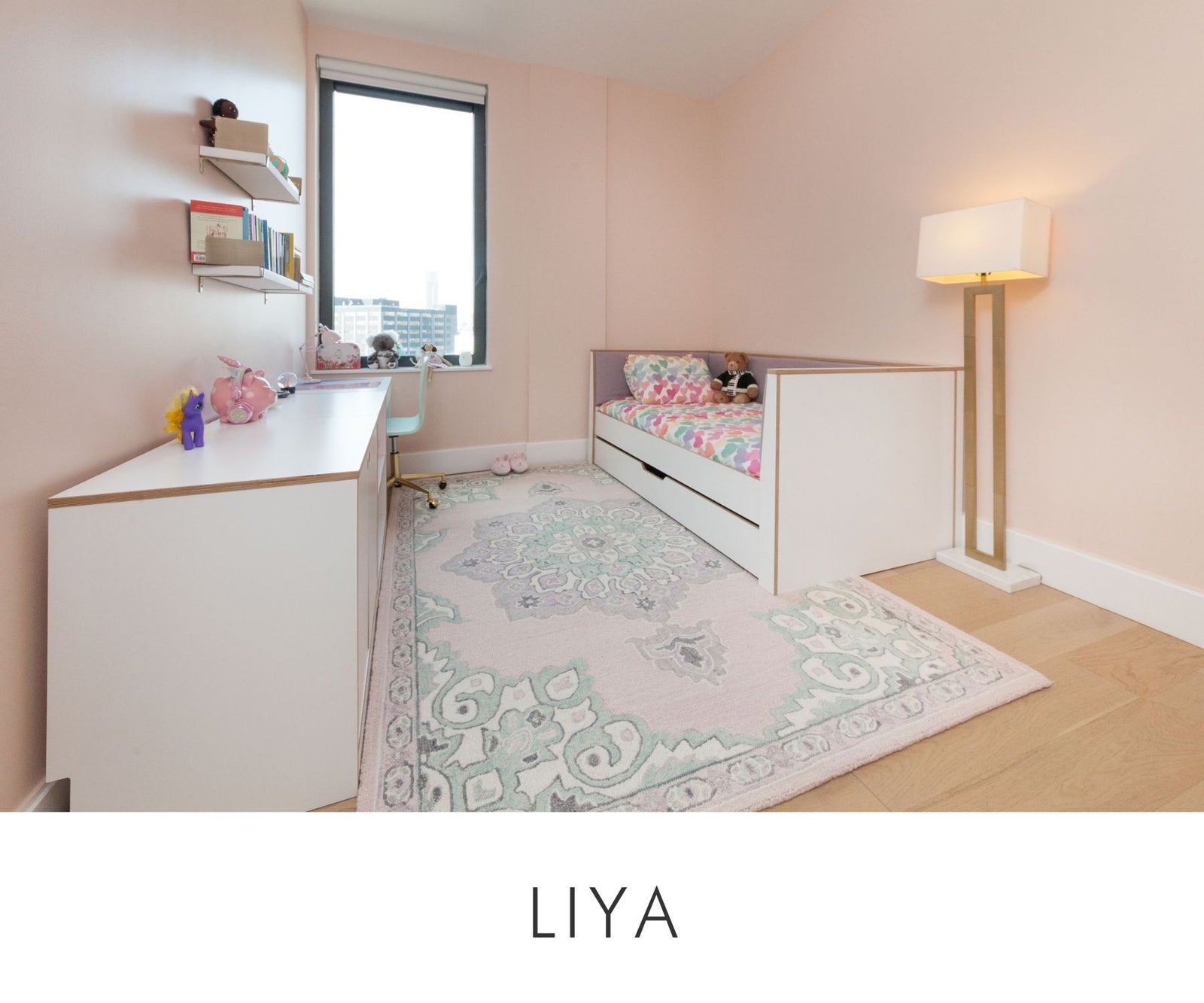 Custom kids daybed with upholstered side panels in a pastel pink room, paired with a white desk and floating bookshelves for a functional children's study and sleep space
