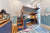 Custom loft bed with integrated desk and storage, featuring a unique artistic design on the loft exterior in blue and wood tones. The staircase includes built-in storage drawers, and the room is decorated with wave-inspired wall art, creating a stylish and functional workspace for kids.

