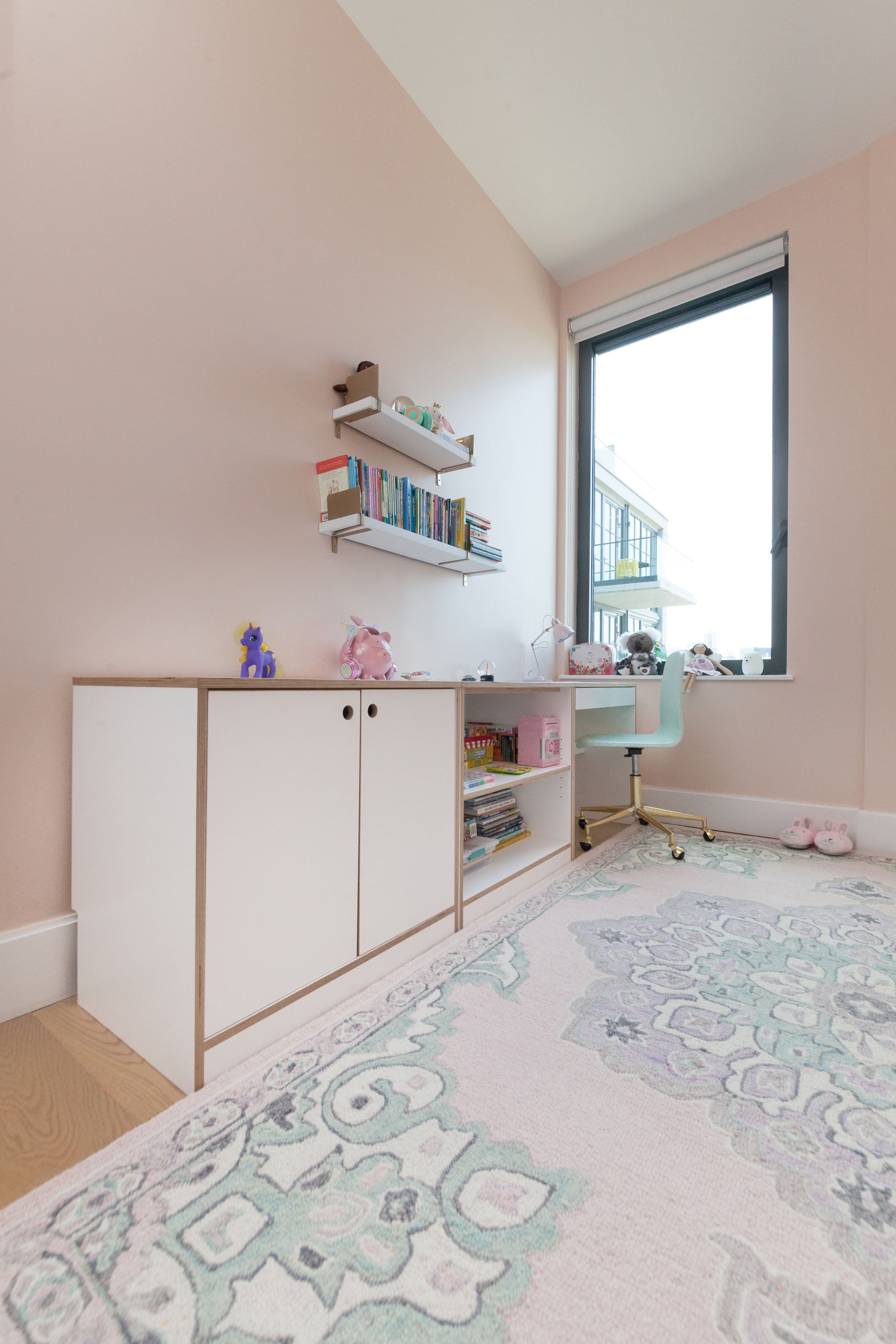 Modular desk with white cabinetry and shelving in a pastel pink bedroom with mint green accents.

