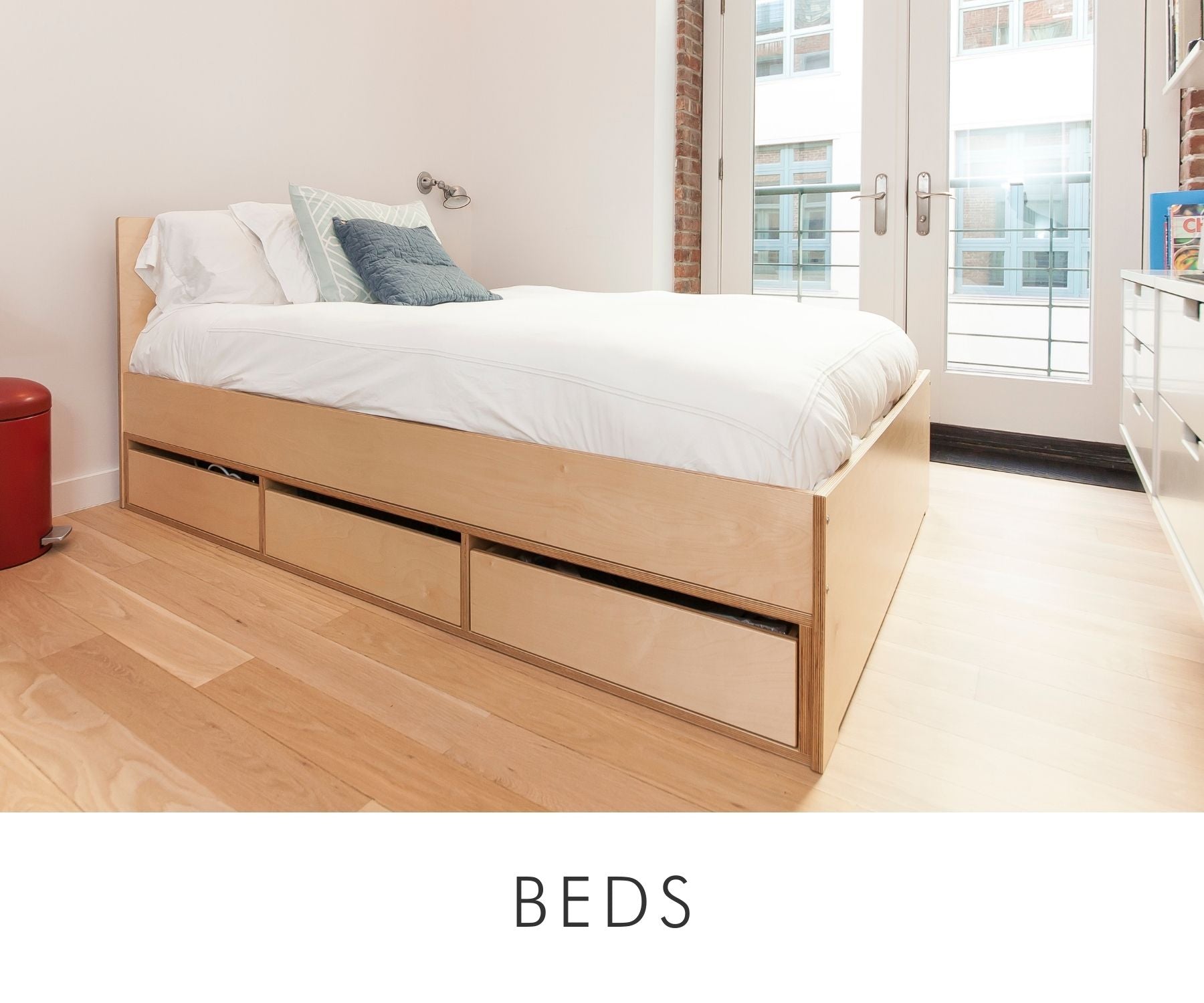 Custom platform bed in natural birch with built-in underbed storage drawers, designed for a compact bedroom with modern furnishings.