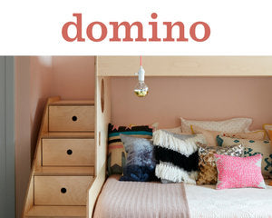 Interior of a cozy bedroom with pink walls, featuring a bed with various decorative pillows and adjacent wooden drawers