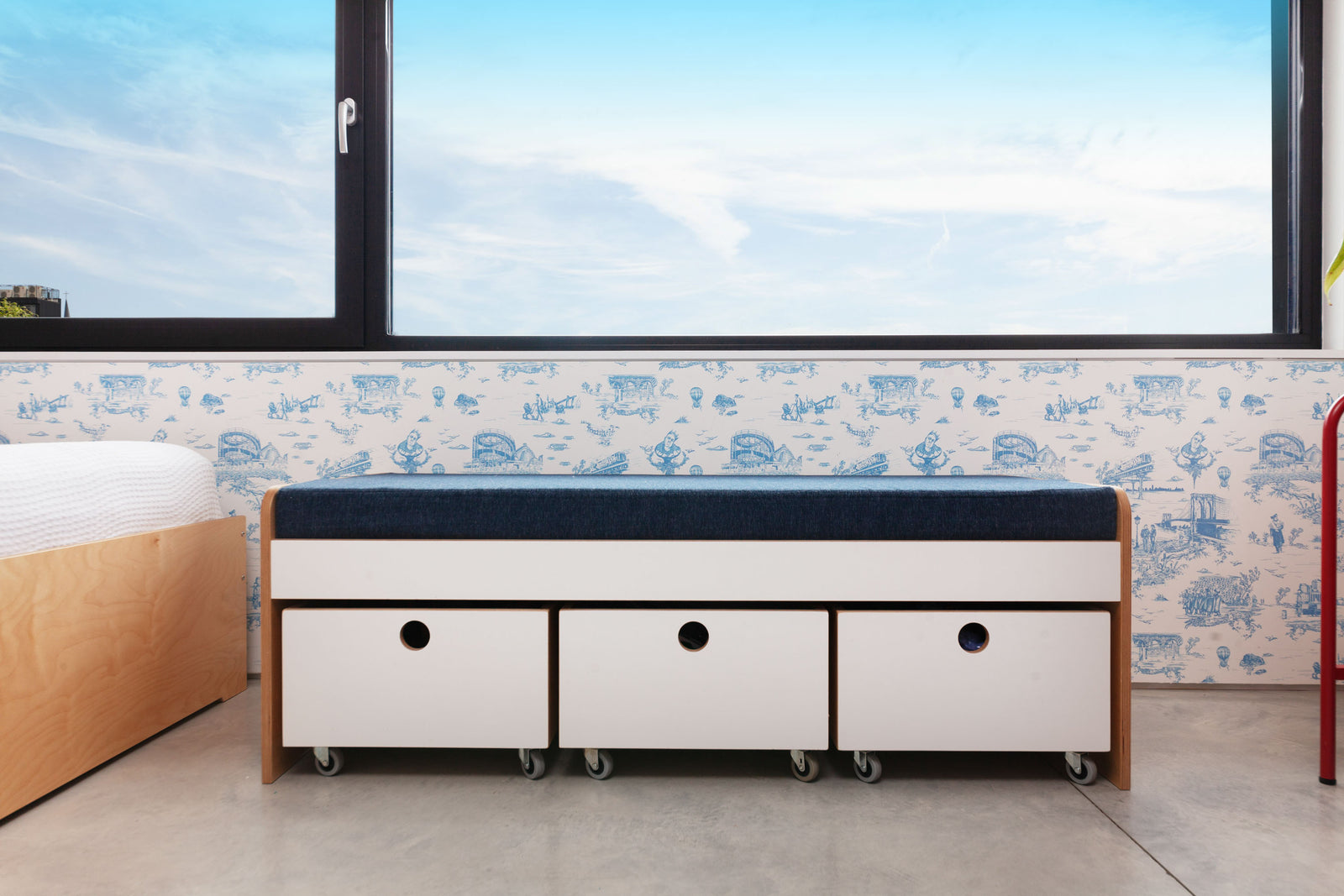 Modular seating bench with white oak finish, white painted accents, and three toy storage carts on casters, under a window in a children's room.

