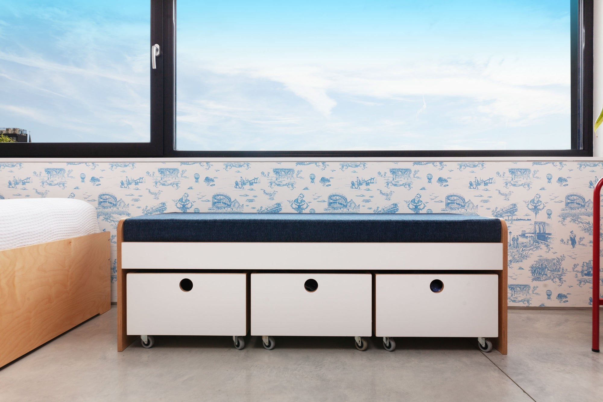 Modular seating bench with white oak finish, white painted accents, and three toy storage carts on casters, under a window in a children's room.

