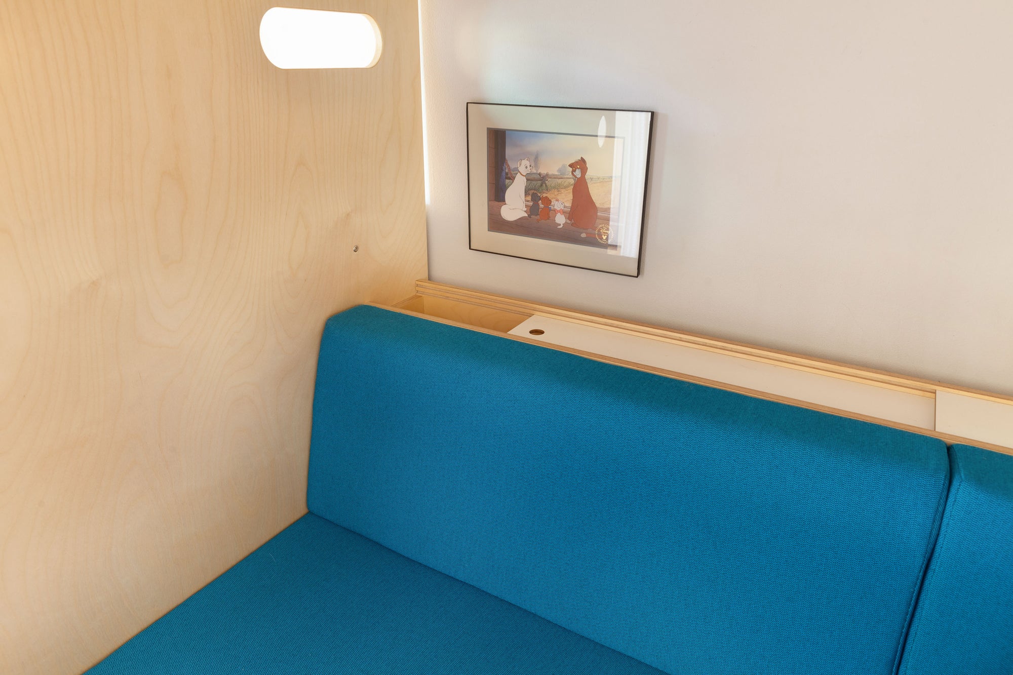 Storage cabinet with sliding doors located behind a blue seating bench under a loft bed, featuring a natural birch finish.

