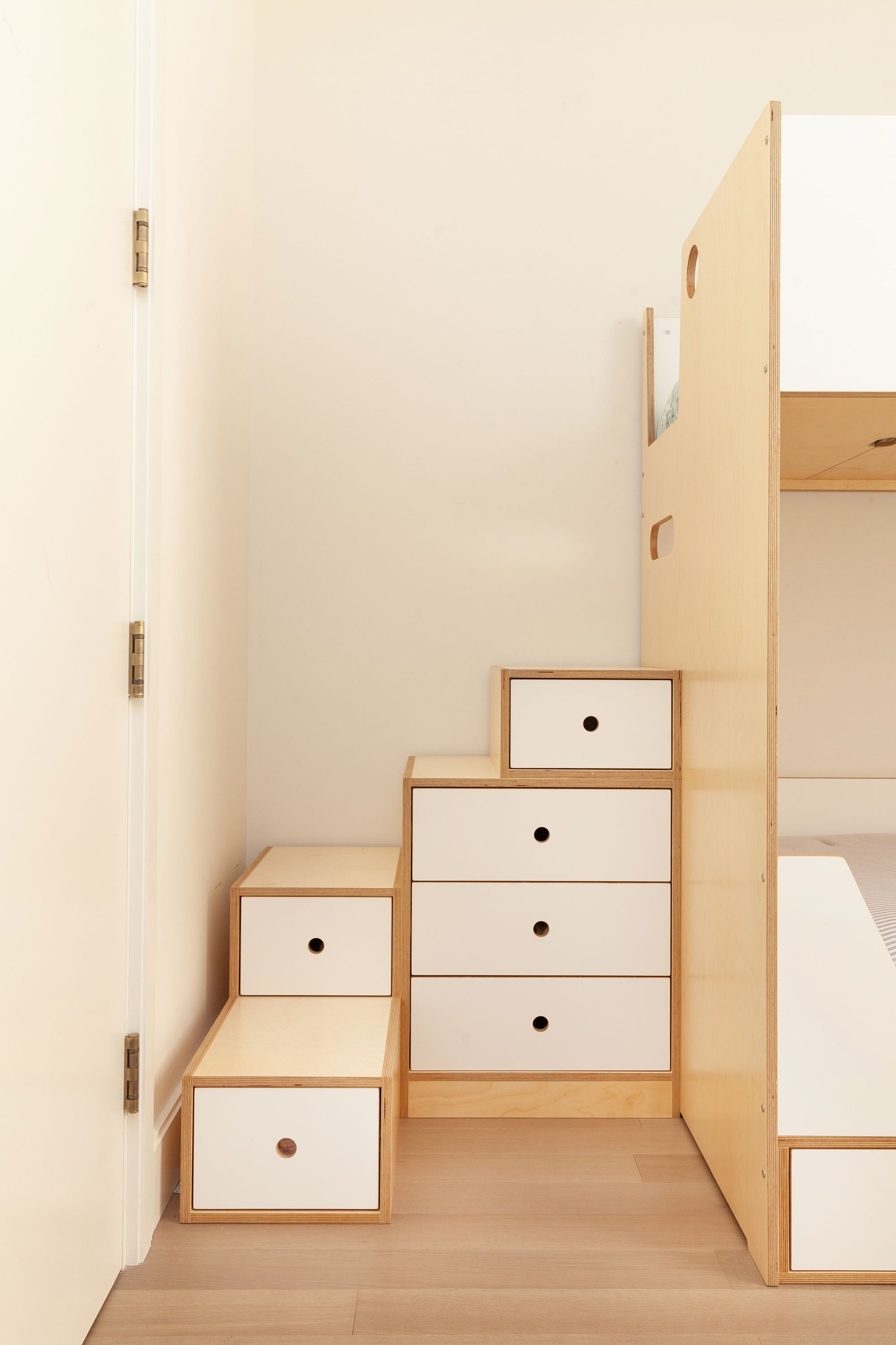 Storage staircase with built-in drawers next to a birch bunk bed, featuring white drawer fronts.

