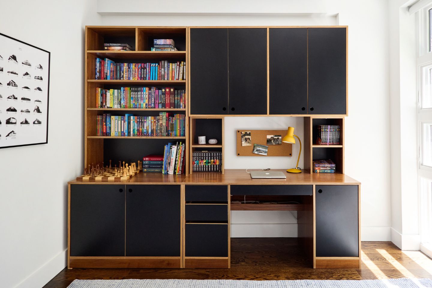 Modulor Desk with black details and dark wood siding attached to matching desk filled with books in white bedroom.