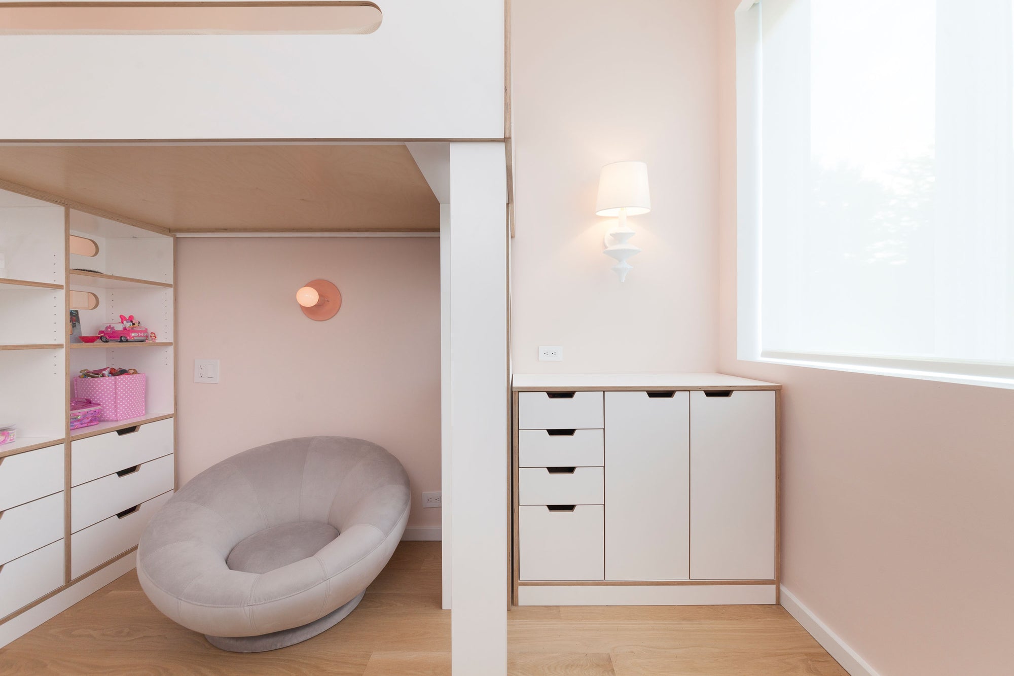 Storage cabinet for art supplies and dresser with white drawers, located under a white loft bed in a light pink room.

