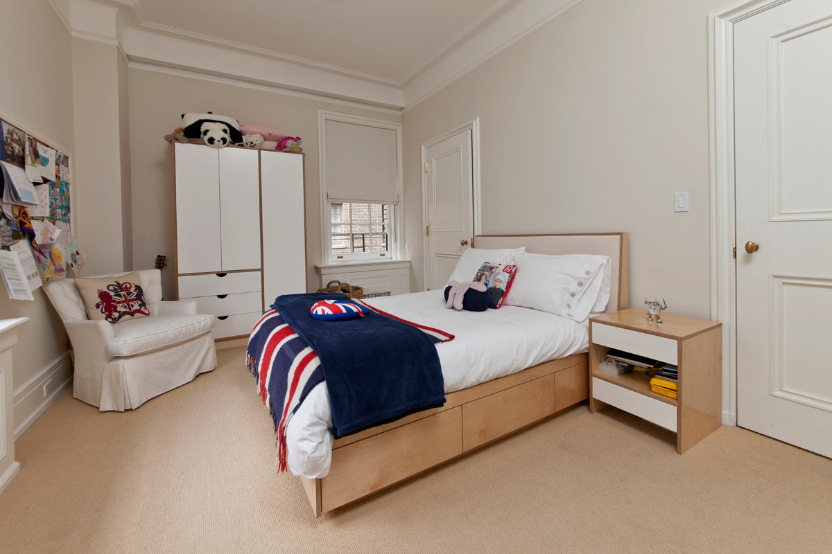 A cozy bedroom with a wooden bed, blue and red blanket, white wardrobe, chair, nightstand, and bulletin board on the wall.