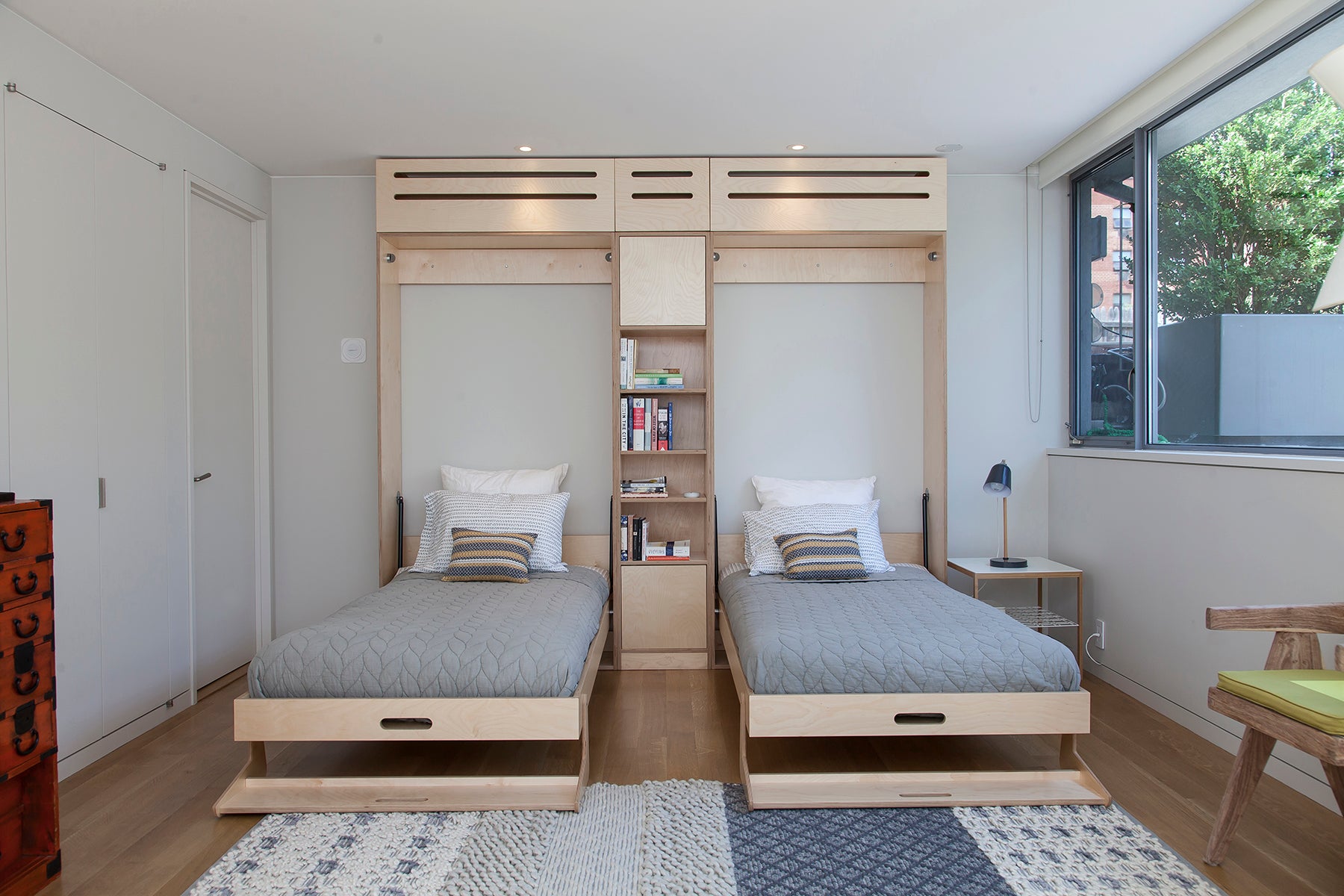 Two twin vertical Tuck Beds in the open position separated by a central wooden bookshelf in a shared bedroom.