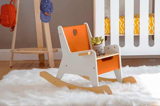 Rockabye Rocker Chair-Casa Kids-Orange and white kids rocking chair with light wood rockers base and storage drawer in seat on a fluffy white carpet in front of white crib in kids room.