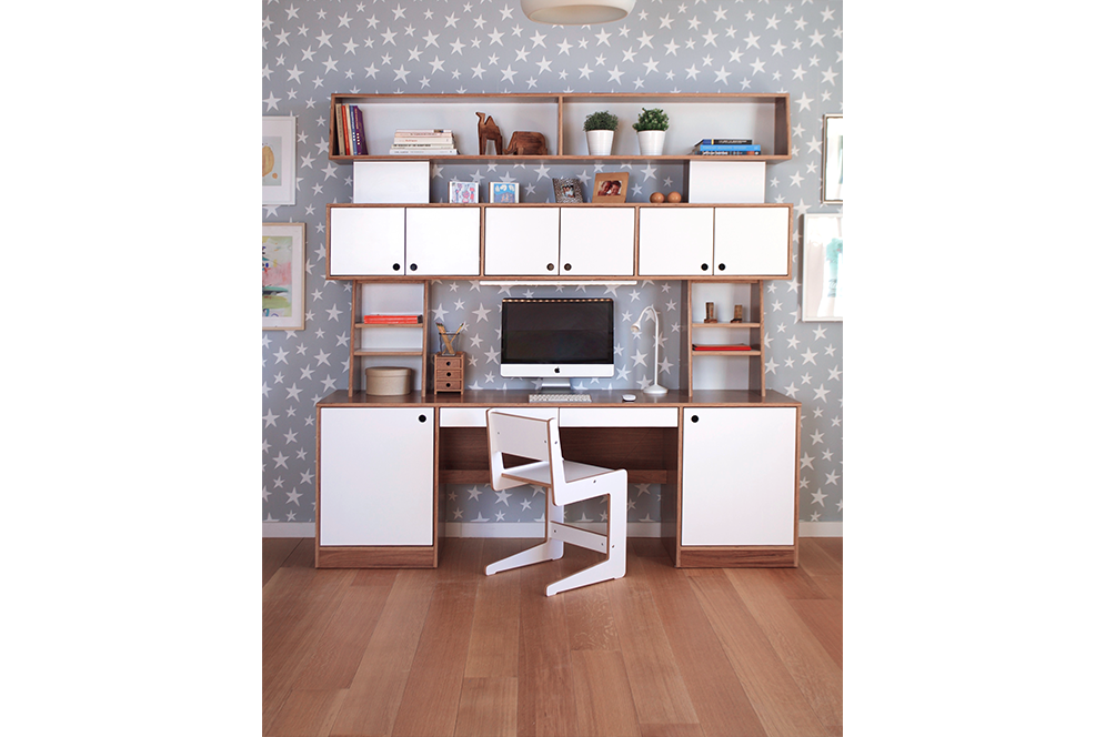 Tall walnut and white desk with many shelves, dual desk drawers on both sides, and white chair against a grey and white stair print wall on wood floor