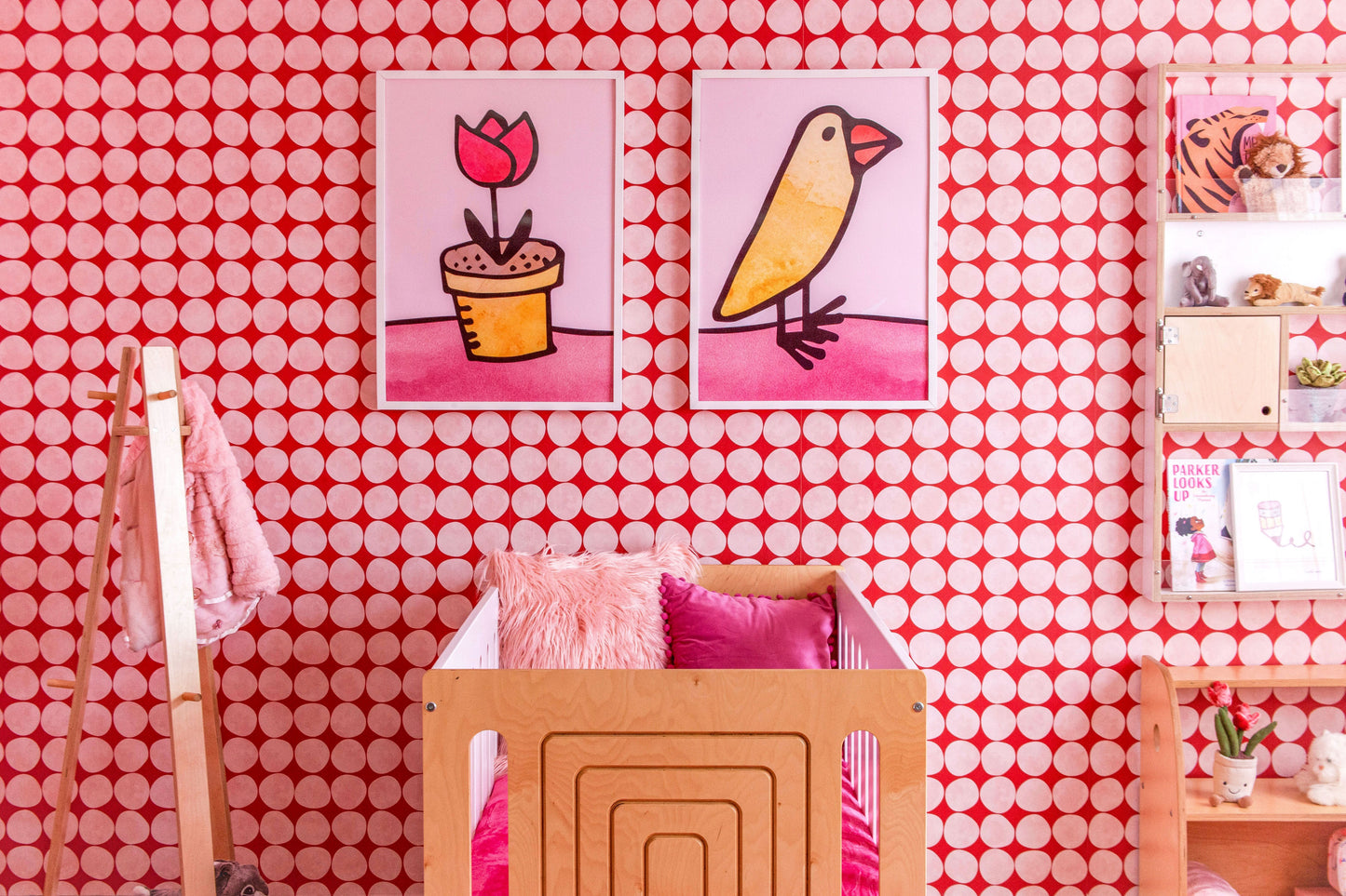 Katie Merz Framed Artwork of a flower pot, baby chick, on pink and white spot wallpaper in kid's room with a light wood crib, pink pillows, and floating light wood shelf.