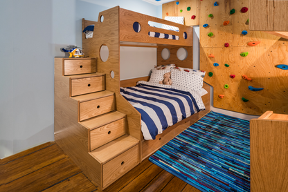 Marino Bunk Bed Twin over Full oak in wooden kid's room with custom rock climbing wall, blue bedding, white walls, and blue rug